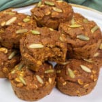 Vegan Pumpkin Ginger Muffins stacked on a gray speckled plate, a bite taken out of 1 muffin