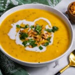 White bowl of butternut squash soup with a green napkin and some roasted pumpkin seeds.