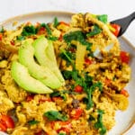 Tofu Scramble on white speckled plate with avocado garnish and black fork lifting bite