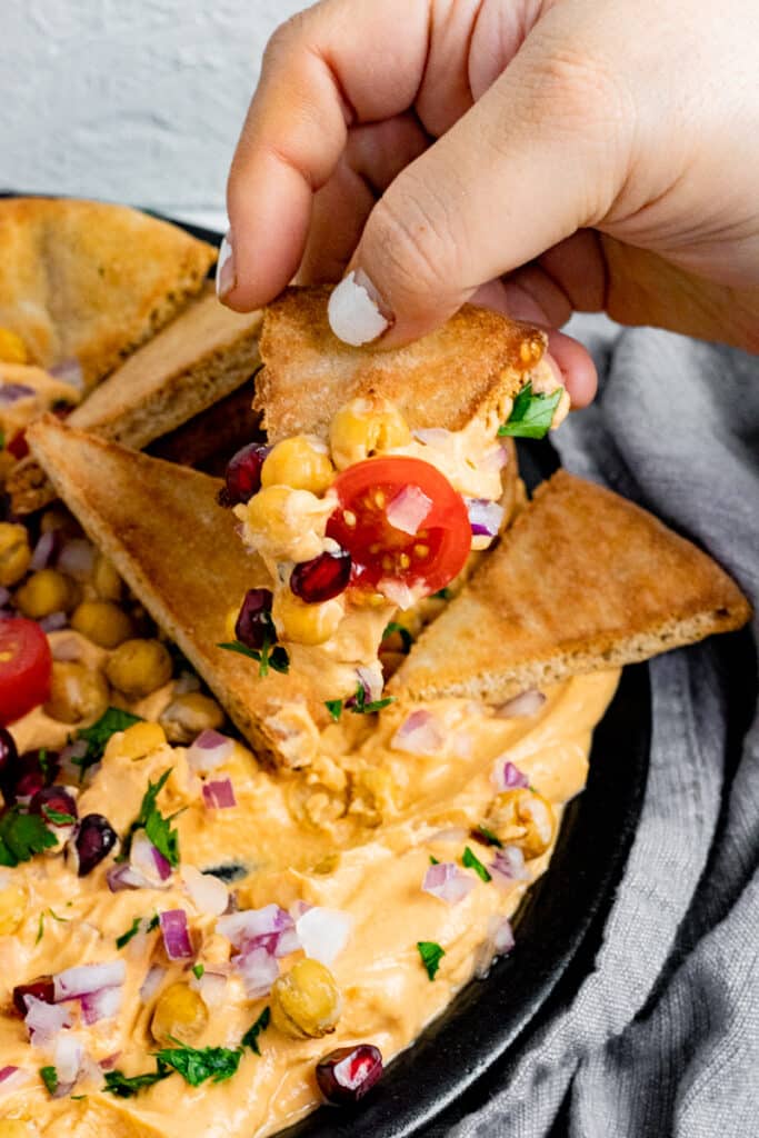 hand dipping pita bread into loaded hummus