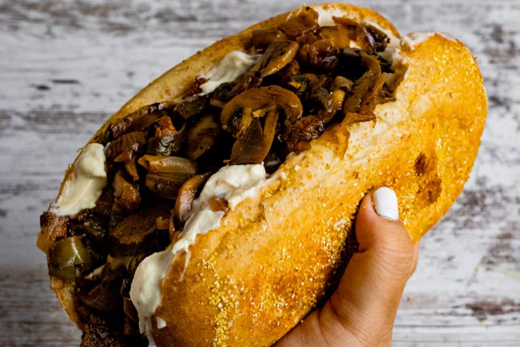 Hand holding a vegan philly cheesesteak
