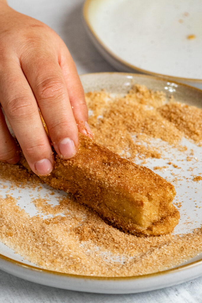 Rolling French Toast Sticks in cinnamon sugar
