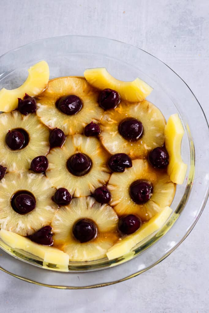 Cherries arranged in between pineapple empty spaces in a pie dish