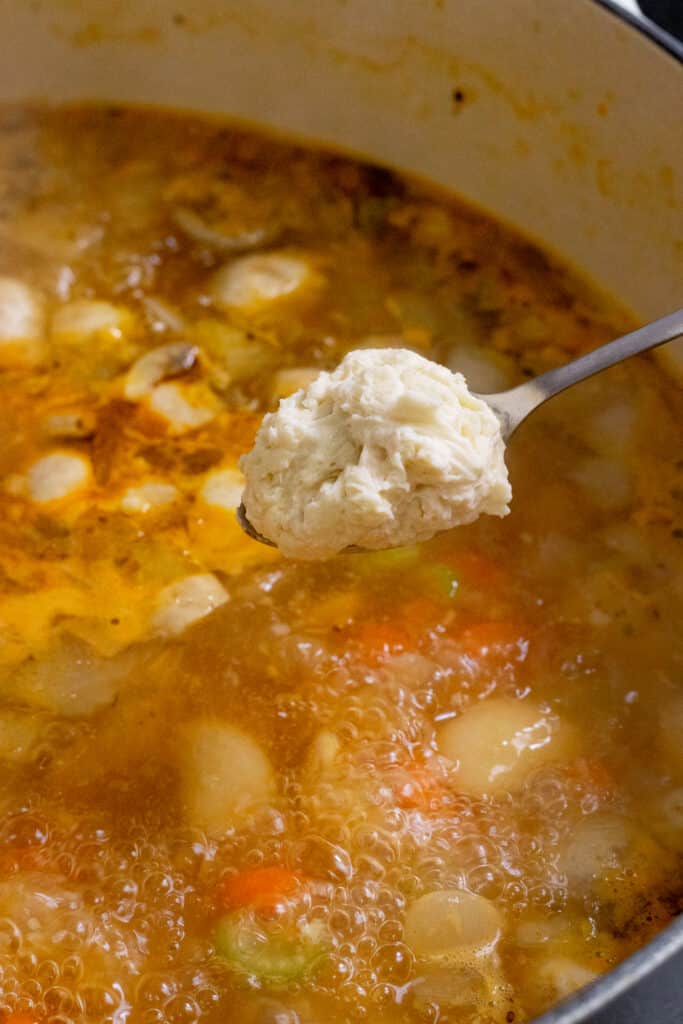 Using a small spoon to add the dumpling dough to the soup