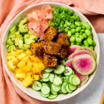 Landscape photo of finished Tofu Poke Bowl in a white speckled bowl with peach napkin and wood chopsticks