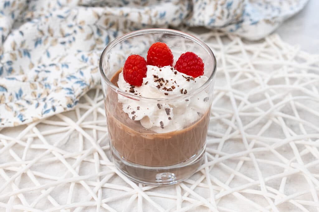 Tofu mousse in a glass with vegan whipped cream and raspberries.