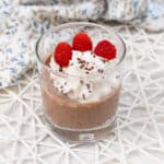 Tofu mousse in a glass with vegan whipped cream and raspberries.
