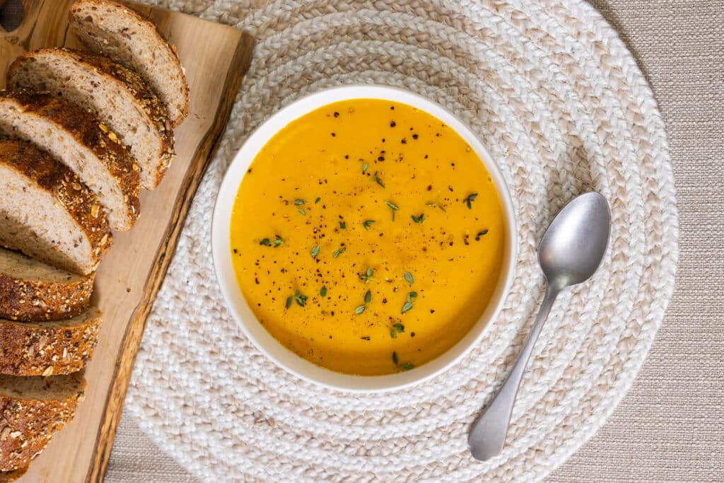 Carrot and Sweet Potato Soup in a bowl with some bread.